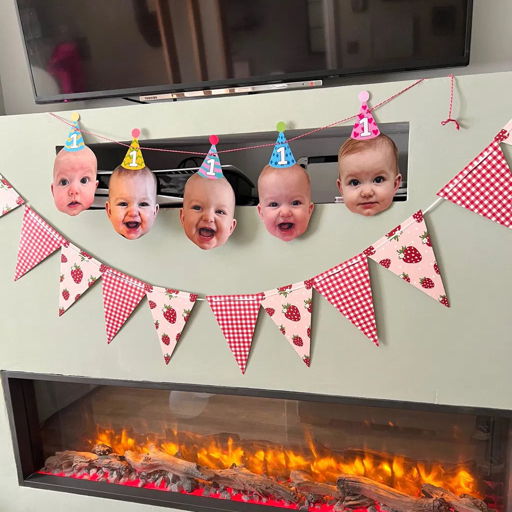 Personalised baby face photo bunting with birthday party hats hanging above a fireplace for a 1st birthday party.