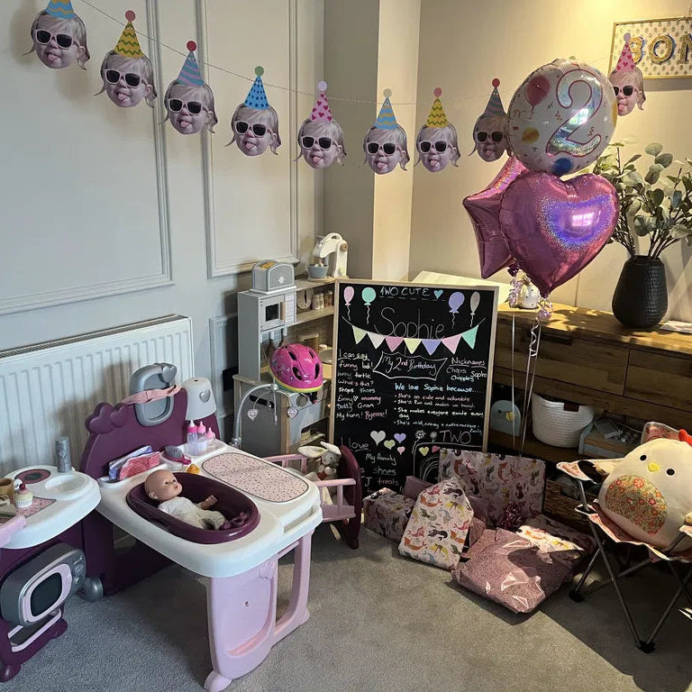 Custom toddler face photo bunting with party hats and sunglasses hanging above a playroom set up for a girl's 2nd birthday party.