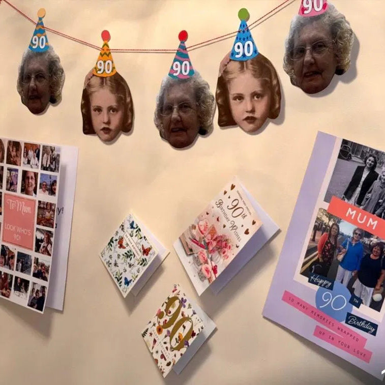 Custom 90th birthday face bunting featuring alternating present-day and childhood throwback photos wearing mini party hats, displayed on a wall above birthday cards.